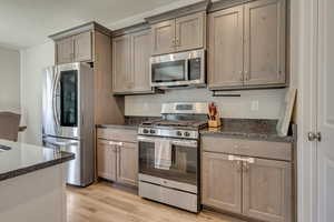 Kitchen featuring stainless steel appliances, light wood-type flooring, dark stone countertops, and gray cabinetry
