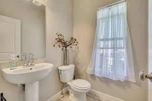 Half bathroom featuring toilet, tile patterned floors, baseboards, and a sink