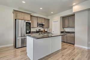 Kitchen featuring appliances with stainless steel finishes, dark stone counters, light wood-style floors, a kitchen island with sink, and recessed lighting