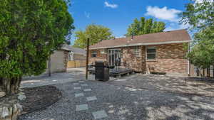 Back of house featuring a deck, a patio, brick siding, and roof with shingles