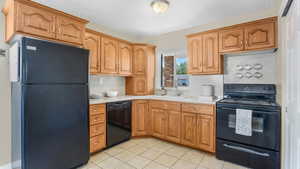 Kitchen featuring black appliances, a sink, light countertops, light tile patterned floors, and a textured ceiling