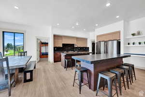 Kitchen with freestanding refrigerator, a kitchen island with sink, dark countertops, a kitchen bar, and recessed lighting