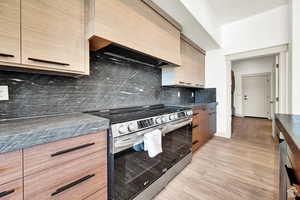 Kitchen with stainless steel electric range, custom range hood, dark countertops, tasteful backsplash, and light wood-style floors