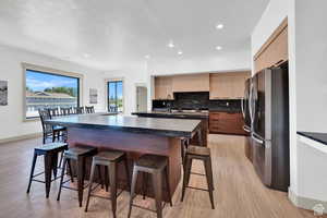 Kitchen featuring freestanding refrigerator, dark countertops, a kitchen bar, modern cabinets, and decorative backsplash