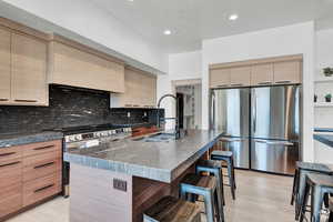 Kitchen featuring a sink, appliances with stainless steel finishes, a breakfast bar, modern cabinets, and tasteful backsplash