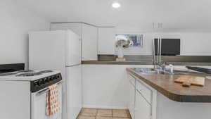 Kitchen featuring white appliances, a sink, white cabinets, and baseboards