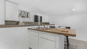 Kitchen featuring a sink, white cabinets, a kitchen bar, carpet, and recessed lighting