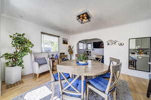 Dining room featuring arched walkways, ornamental molding, a textured ceiling, light wood-style floors, and baseboards