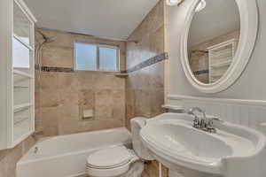 Travertine tile full bathroom with shower / bath combination with curtain rod, a sink, and toilet
