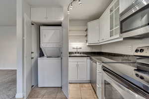 Kitchen featuring appliances with stainless steel finishes, stacked washer and dryer, a sink, white cabinets, and glass insert cabinets