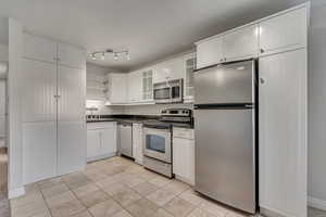 Kitchen featuring appliances with stainless steel finishes, granite countertops, open shelves, a sink, and light travertine floors with laundry doors closed