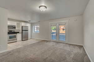 Open floor plan with Kitchen, Dining and Living Room, light colored carpet and travertine tile floors, glass insert cabinets, white cabinetry, and Juliet balcony