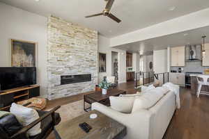 Living room with a ceiling fan, a stone fireplace, dark wood-style floors, recessed lighting, and baseboards