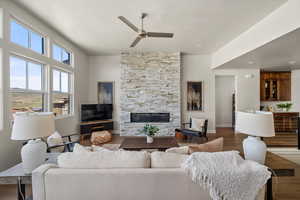 Living area with ceiling fan, a stone fireplace, wood finished floors, baseboard heating, and baseboards
