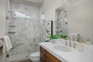 Bathroom featuring vanity, toilet, and a marble finish shower