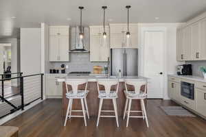 Kitchen featuring wall chimney exhaust hood, freestanding refrigerator, tasteful backsplash, light countertops, and dark wood-style floors