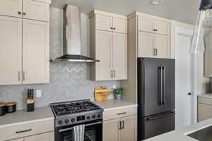 Kitchen featuring wall chimney exhaust hood, high end refrigerator, range with gas stovetop, and light countertops