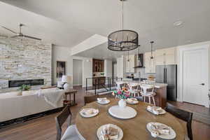 Dining room featuring dark wood-type flooring, ceiling fan, a stone fireplace, recessed lighting, and baseboards
