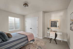 Carpeted bedroom with baseboards, an office area, and a closet