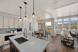 Kitchen with a sink, light countertops, tasteful backsplash, dark wood-style floors, and hanging light fixtures