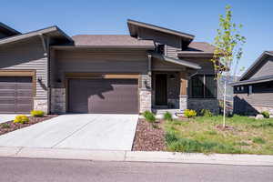 View of front of property featuring a garage, concrete driveway, stone siding, and a shingled roof