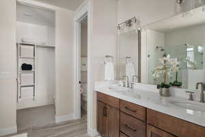 Bathroom with toilet, a shower stall, double vanity, wood finish floors, and baseboards