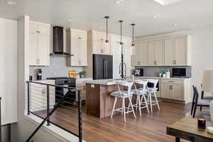 Kitchen featuring wall chimney exhaust hood, high quality fridge, gas stove, a kitchen island with sink, and recessed lighting