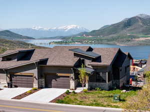 View of front of home featuring stone siding, a water and mountain view, a garage, concrete driveway, and roof with shingles