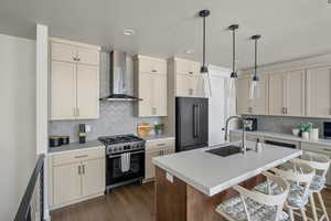 Kitchen featuring wall chimney exhaust hood, high end refrigerator, a sink, gas range, and tasteful backsplash