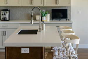 Kitchen with a sink, wood finished floors, decorative backsplash, light countertops, and baseboards