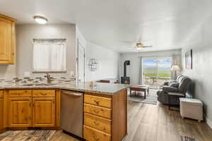Kitchen with stainless steel dishwasher, a sink, a wood stove, light wood-type flooring, and open floor plan
