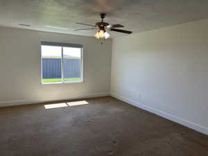 Carpeted spare room with baseboards, ceiling fan, and a textured ceiling