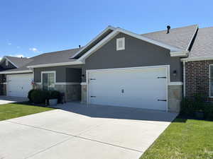Ranch-style home featuring a shingled roof, an attached garage, concrete driveway, stone siding, and stucco siding