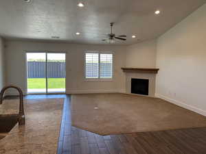 Unfurnished living room featuring dark wood-type flooring, a ceiling fan, baseboards, a tiled fireplace, and a sink