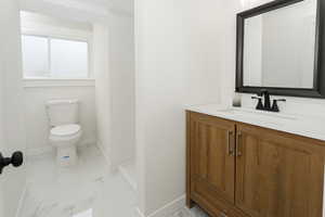 Bathroom featuring baseboards, marble look tiles, toilet, vanity, and a shower