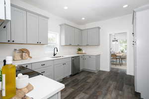 Kitchen with stainless steel dishwasher, a sink, gray cabinetry, dark wood-style flooring, and light countertops