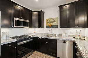 Kitchen featuring stainless steel appliances, light wood-type flooring, and light stone countertops