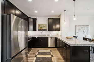 Kitchen featuring appliances with stainless steel finishes, a breakfast bar area, a peninsula, light wood-style flooring, and pendant lighting