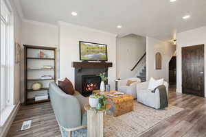 Living area with wood finished floors, crown molding, a tile fireplace, recessed lighting, and stairs