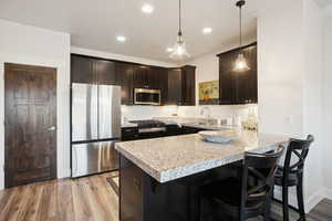 Kitchen featuring stainless steel appliances, a peninsula, a kitchen bar, dark brown cabinets, and recessed lighting