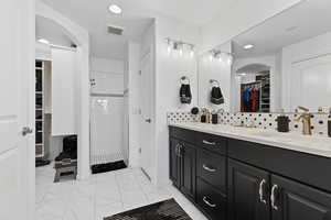 Bathroom with double vanity, a tile shower, a walk in closet, marble look tiles, and tasteful backsplash