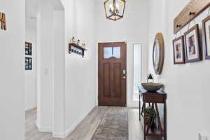 Foyer with arched walkways, light wood-type flooring, baseboards, a chandelier, and a towering ceiling