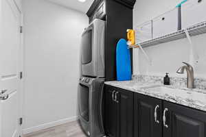 Laundry area with stacked washing machine and dryer, light wood-style flooring, cabinet space, and baseboards