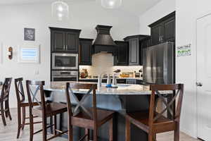 Kitchen featuring stainless steel oven, built in microwave, dark cabinets, custom range hood, and a breakfast bar area