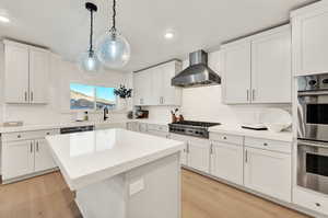 Kitchen featuring wall chimney exhaust hood, appliances with stainless steel finishes, a sink, backsplash, and light wood-style floors
