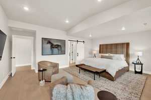 Bedroom with a barn door, baseboards, recessed lighting, wood finished floors, and vaulted ceiling