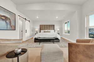 Bedroom featuring a barn door, multiple windows, vaulted ceiling, baseboards, and wood finished floors