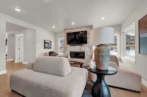 Living area featuring plenty of natural light, baseboards, a stone fireplace, wood finished floors, and recessed lighting
