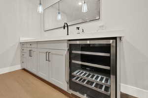 Bar featuring beverage cooler, light wood finished floors, baseboards, and decorative light fixtures