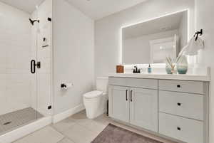 Bathroom featuring vanity, a stall shower, toilet, baseboards, and tile patterned floors